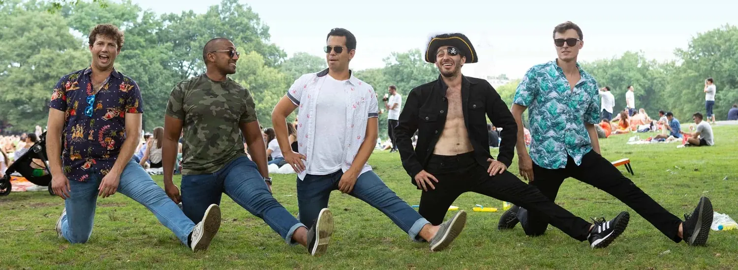Five men in denim posing on a park lawn